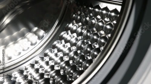 Washing machine drum closing with automatic door. Detailed close-up shot of an empty washing machine's shiny stainless steel drum with a modern hexagonal pattern as the automatic door slowly closes