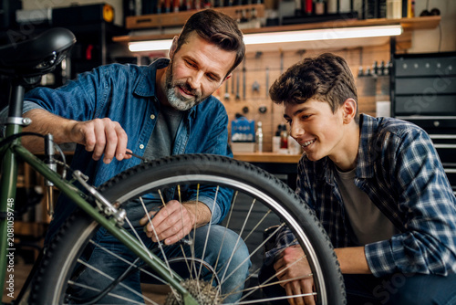 Pai ensinando filho adolescente a consertar bicicleta em uma garagem - Conceito de legado, mentoria, trabalho em equipe e tempo de qualidade.