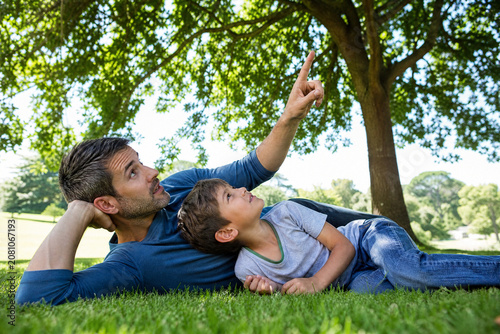 Pai e filho deitados na grama sob a sombra de uma árvore em um parque ensolarado - Conceito de relaxamento, tempo de qualidade e conversa entre pai e filho.