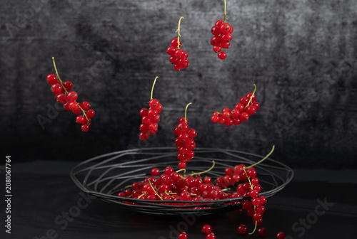 Fresh red currants are lying in a metal basket. The background is dark. More currants are falling into the basket from above.