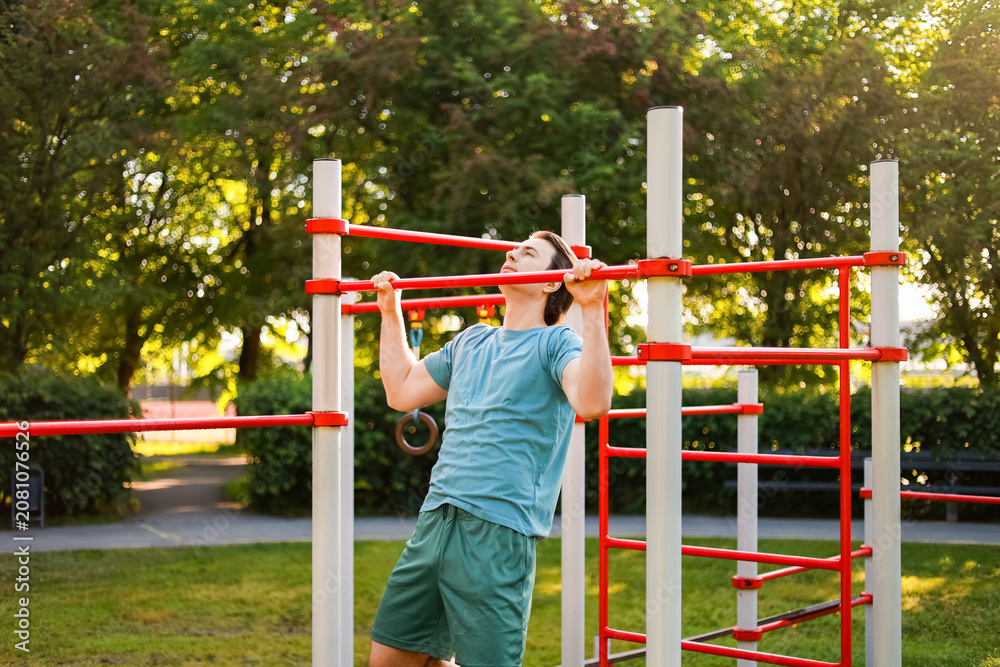 Obraz premium man doing a pullup exercise on a bar during an outdoor workout in a sunny park. Sport, fitness and strength training for a healthy lifestyle.