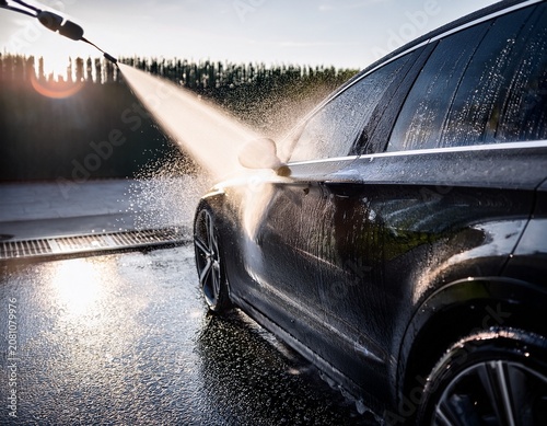 close up of a sleek dark car receiving a heavy water spray during washing