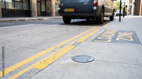 Circular wireless in-ground electric vehicle charging pad installed on a city street loading zone with a van parked nearby