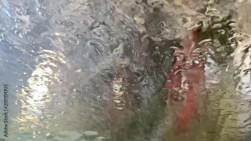 Conveyor car wash process, view from inside the vehicle: the start of the wash with foam and the blurred silhouette of the car ahead.
