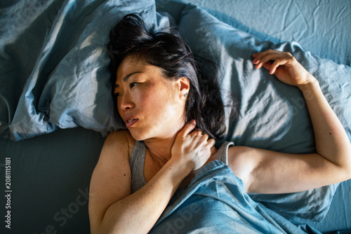 Woman with neck pain awake in bed at home
