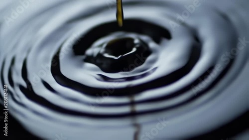 Close-up of water's surface as a drop impacts, creating concentric ripples. Light and shadow interplay