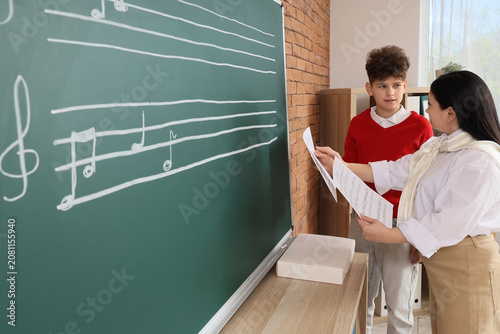 Teenage boy with teacher learning music notes near blackboard in classroom