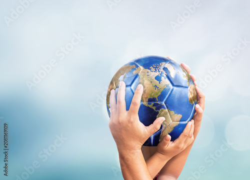 Hands holding planet earth globe soccer ball on soft blue bokeh background for global sports and peace concept design