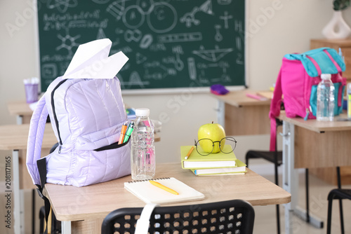 Photos Apple with eyeglasses, books and backpack on desk in classroom