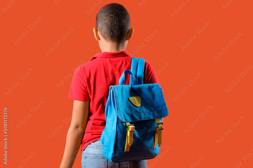 Obraz premium Little schoolboy with backpack on orange background, back view