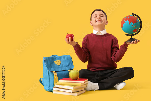 Little schoolboy with apple and globe sitting on yellow background