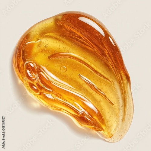 A glossy, amber-colored viscous liquid drop with smooth textures and light reflections on a neutral background