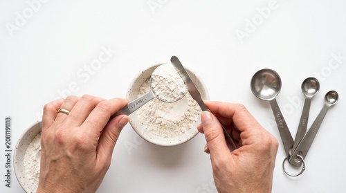 Photorealistic close-up hands measuring ingredients with spoons, cooking prep, isolated on pure white background