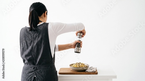 Photorealistic person viewed from behind, no face visible, grinding pepper over dish, simple action, white isolated background