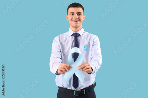 Young businessman with blue ribbons on color background. Prostate cancer awar...