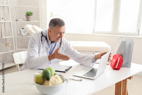 Mature doctor video chatting with patient on laptop in office