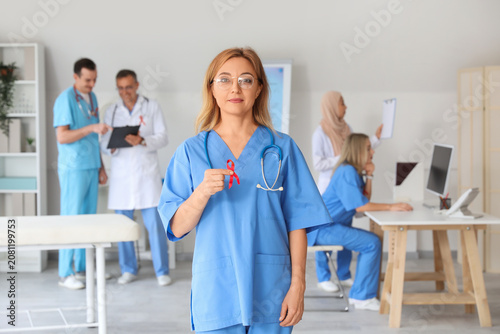 Mature female doctor with red ribbon in clinic. World AIDS Day concept