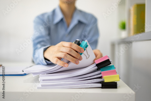Professional woman organizes documents with colorful clips. She holds a marker, ready to annotate papers. Stacked sheets and vibrant clips add visual interest. Focused demeanor suggests productivity
