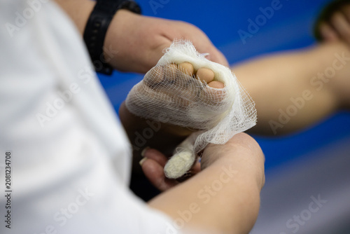 Close-up view of a sports injury on a kickboxer’s foot, with visible trauma on the toes and forefoot. A medical worker carefully applies a bandage, wrapping the injured area to provide support 