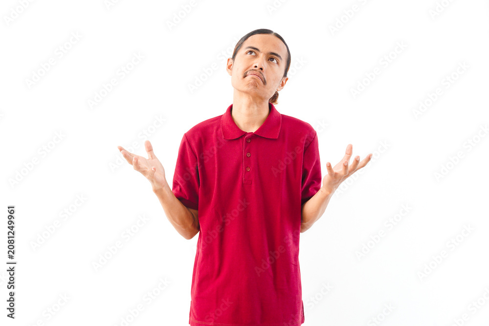 Naklejka premium Portrait of an Asian man with long hair wearing a red shirt, making an angry and frustrated gesture against a plain white background.