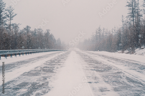 Foto Snow-covered highway through forest during intense winter storm in daytime