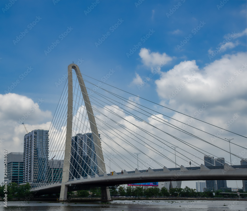 Obraz premium Modern Cable-Stayed Bridge Over a River With City Skyline and Blue Cloudy Sky