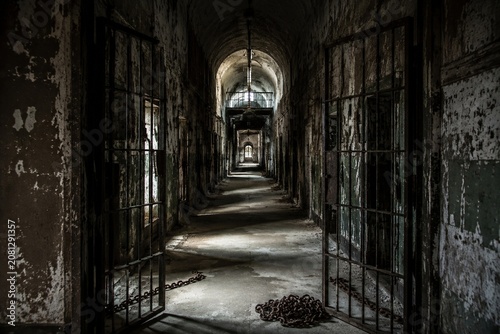 An empty prison corridor with open iron doors and chains on the floor.