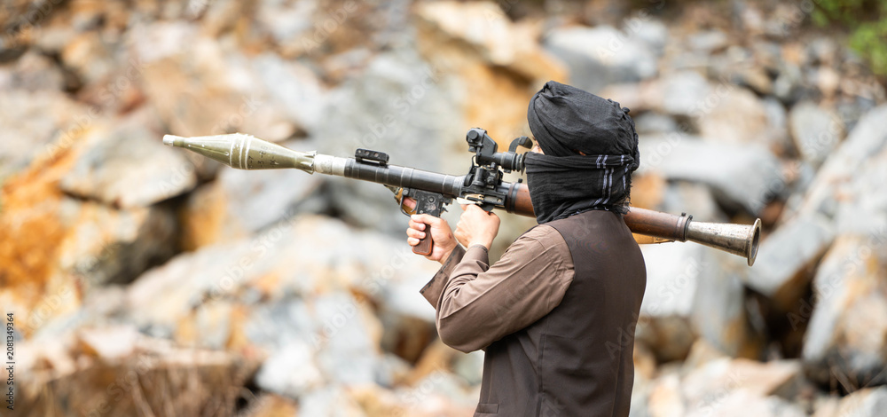 Fototapeta premium Armed militant aiming a rocket launcher during a simulated conflict scenario in rocky outdoor terrain