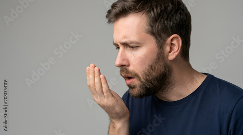 Side view of man checking his breath with hand over mouth