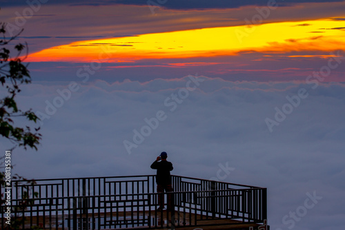 A silhouette of a man standing on a rooftop taking pictures of the sea of ​​fog in the morning.