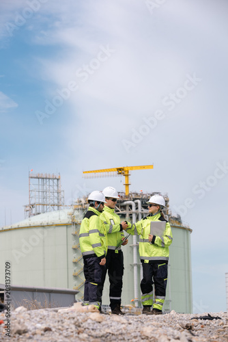 Team of engineers working together at a refinery with industrial structures in the background