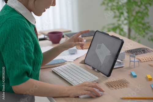 A close up of a designer's hand pointing at a 3D furniture render displayed on a tablet propped up on her desk.
