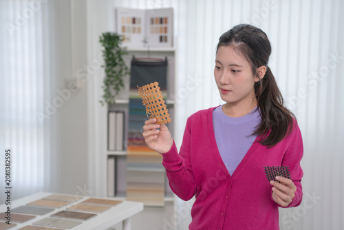 A young designer closely inspects a woven cane texture sample held up in her hand while another sample rests in her other hand.
