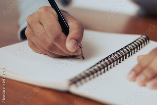Close up of a womans hand jotting down notes in a spiral notebook on a rustic wooden table