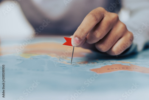 Womans hand delicately places a red marker flag on a world map highlighting a specific location