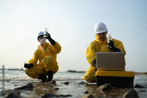 Two focused scientist in yellow protective suit working on water sample analysis. biologist and ecologist researching environmental pollution and contamination outdoors