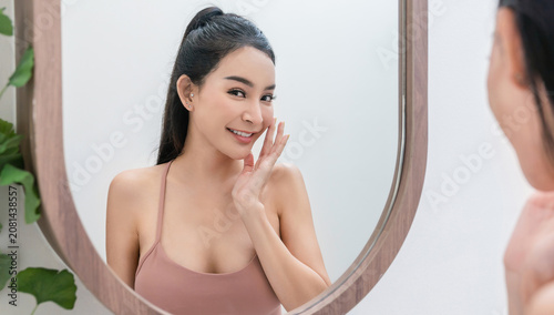 Portrait of young beautiful sexy asian woman applying skincare looking in mirror bathroom. Smile happy face asian girl. Beauty treatment perfect clear skin makeup spa asia lifestyle
