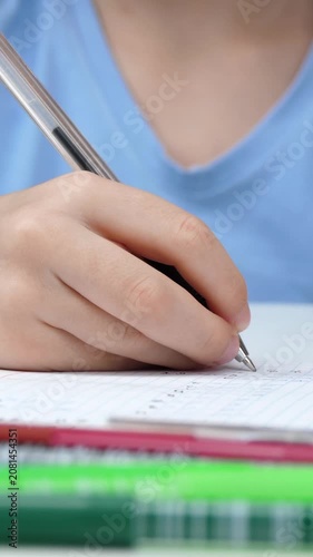 Close-up of child hands writing in notebook with pen during study session. Vertical video captures learning process, concentration and everyday education in calm home environment.