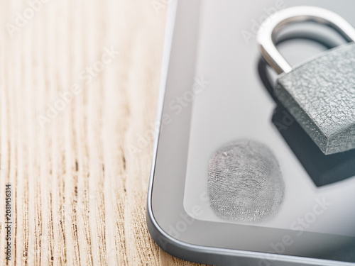 Close up of padlock and fingerprint on digital tablet screen on wooden table, modern cybersecurity concept for digital trust, data privacy, biometric authentication, secure access, online identity