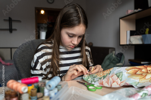 Obraz na plátně Girl embroidering with threads while sitting at table with sewing supplies