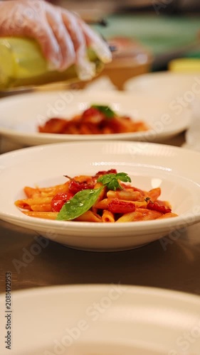 Pouring olive oil from a dispenser bottle over a freshly plated dish of penne pasta. Plating  dishes in a luxury restaurant.