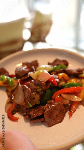 Waiter's hand reaching up to carry a freshly prepared plate of beef stir-fry from the kitchen pass to a restaurant dining table. Waiter carrying a dish from the kitchen to the table.