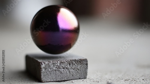A shiny black ball with purple and pink hues is suspended in mid-air, balanced on a gray block.