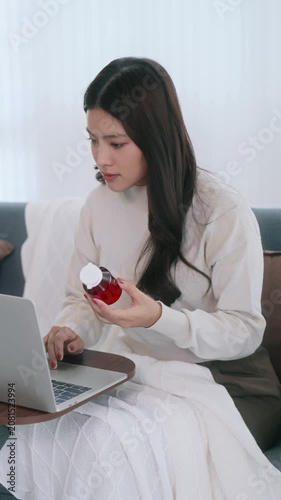 Asian woman holding drug bottle reading information on laptop at home