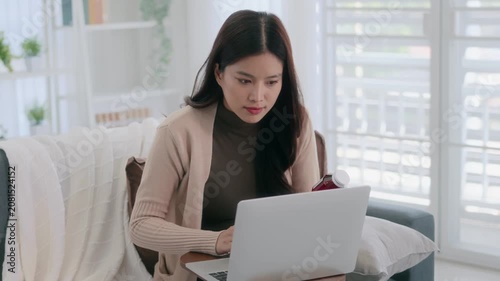 Asian woman holding drug bottle reading information on laptop at home