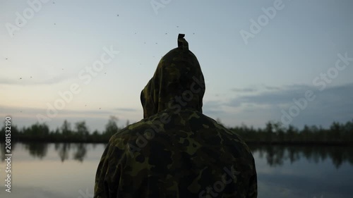 Hooded Figure in Camouflage by a Quiet Lake at Dusk