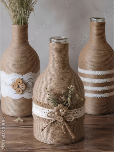 Glass bottles are stylishly upcycled and wrapped in natural jute twine. Each bottle features unique embellishments, including delicate white lace, wooden buttons, and burlap trim.