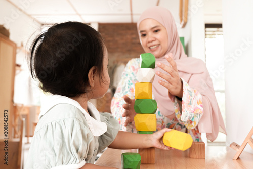 Muslim mother helping toddler build colorful wooden block tower at home