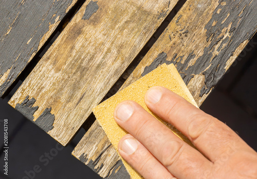 Man sanding loose peeling black paint off a wooden outdoor patio table. Garden DIY chore concept