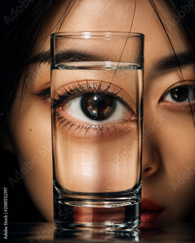 Surreal Portrait of an Asian Woman with an Eye Magnified Through a Glass of Water
